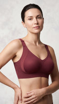 A woman modeling a ribbed, wireless bra in a deep burgundy color against a textured light gray background.