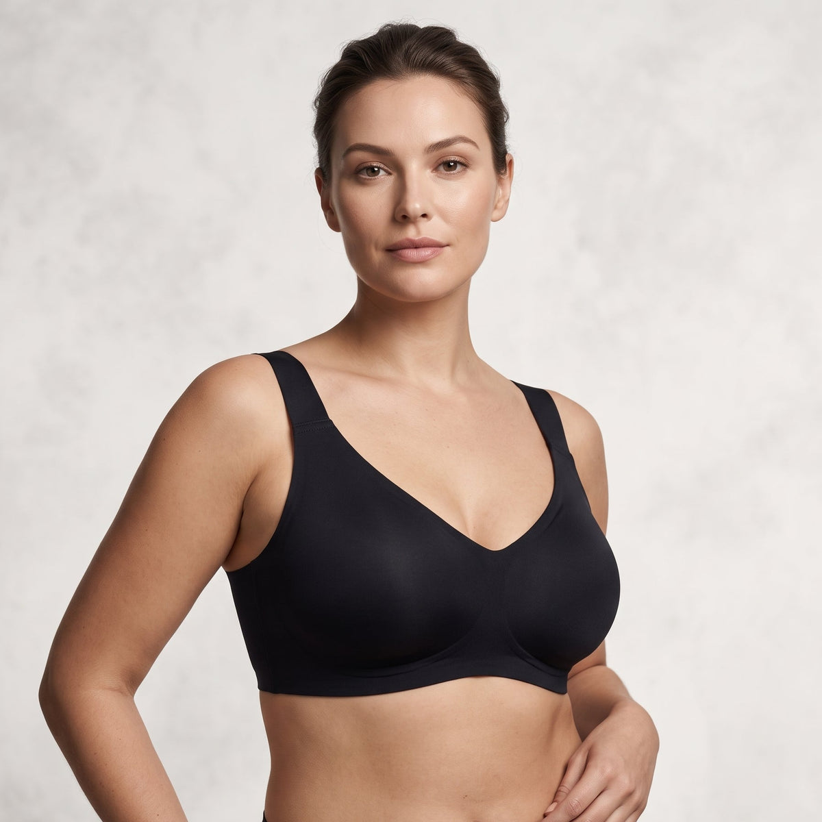 A woman modeling a black wireless bra and matching black underwear against a light gray textured studio background.