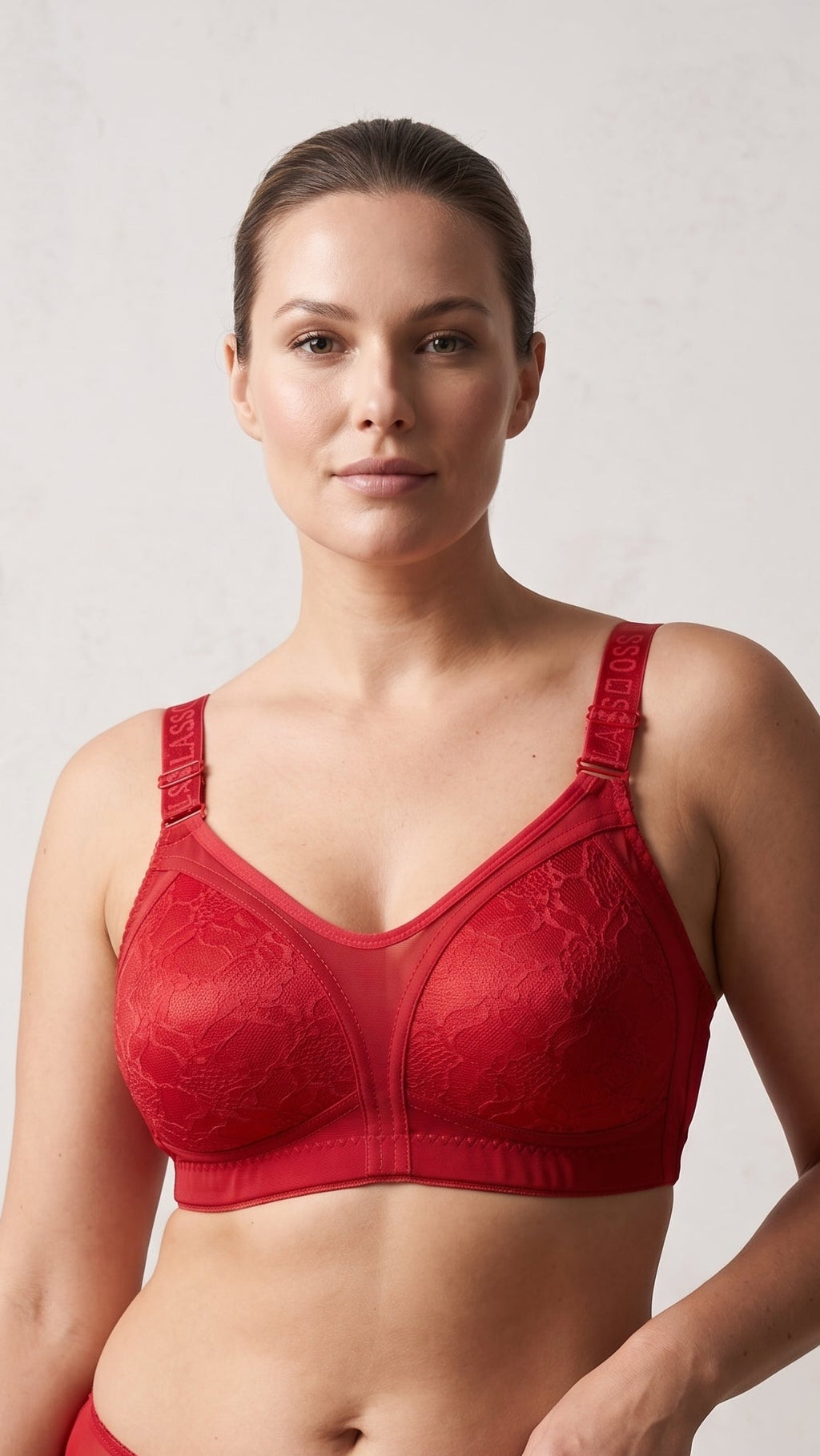 A woman modeling a red lace underwire bra against a light gray studio background.