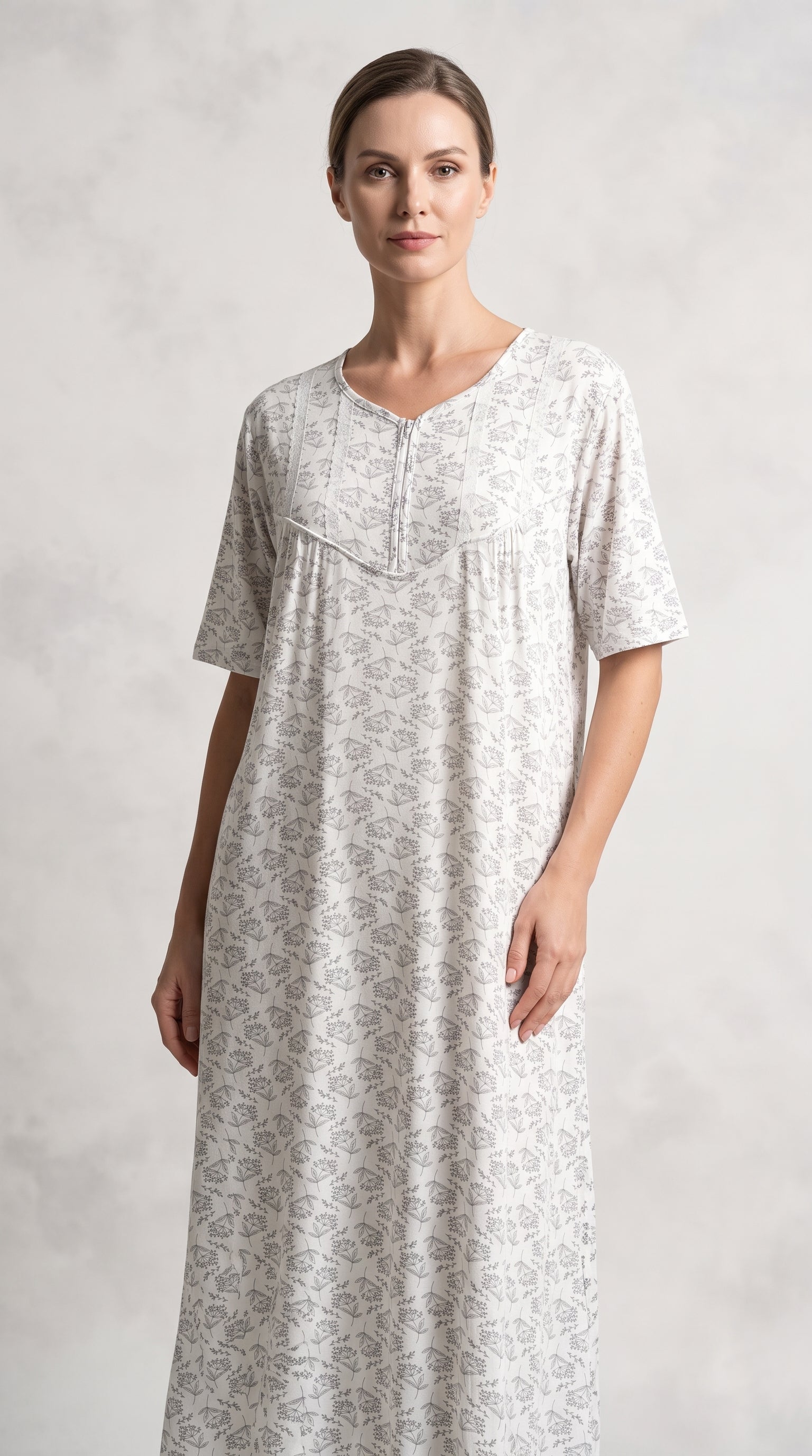 A woman modeling a short-sleeved, knee-length nightgown with a delicate beige floral pattern on a white background, set against a neutral gray studio backdrop.