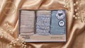 A boxed set of three pairs of women's underwear displayed in a gift box on draped champagne satin with baby's breath flowers. The set includes a light taupe glitter pair, a light blue floral print pair, and a light blue star print pair.