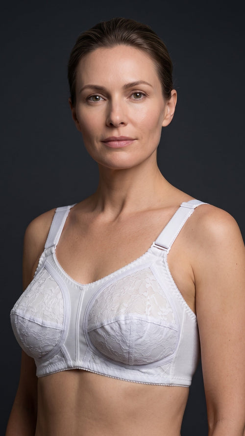 A woman modeling a white lace underwire bra against a dark gray studio background.